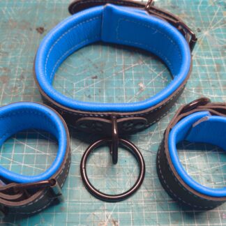 A set of two leather cuffs and collar, with bright blue lining and black straps. The hardware is also black.